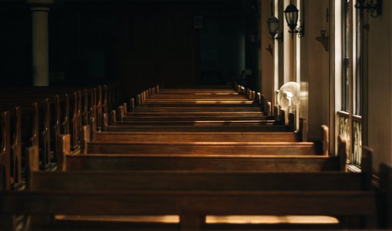 Rows of empty wooden church pews lit by sunlight from side windows.