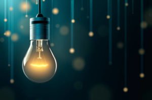 An illuminated light bulb hanging in front of softly glowing lights.