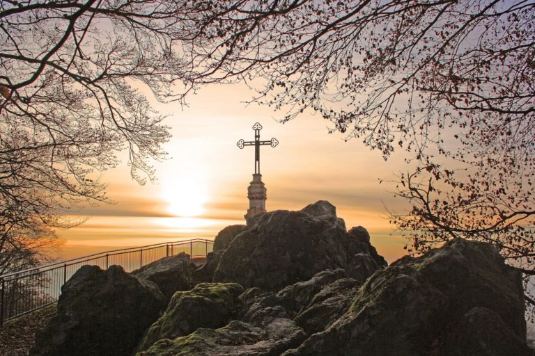 A cross on a rocky hill beneath a golden sky.