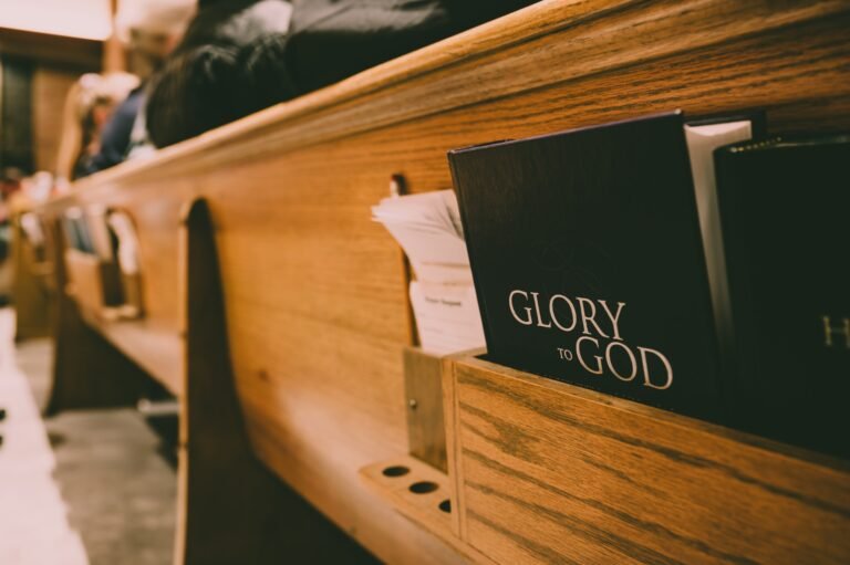 A “Glory to God” hymnal in the book rack of a wooden church pew.