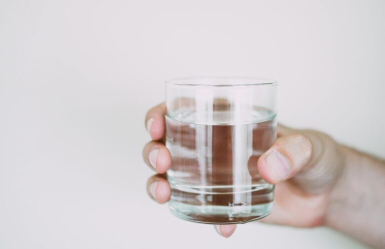 A hand holding a clear glass of water.